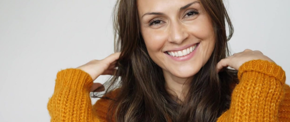 Smiling Woman wearing a mustard yellow sweater against a plain background